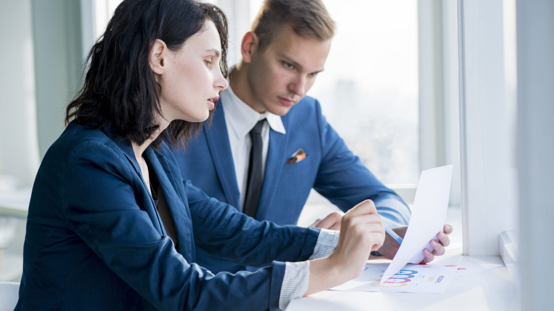 two-businesspeople-examining-chart-at-workplace-1-1